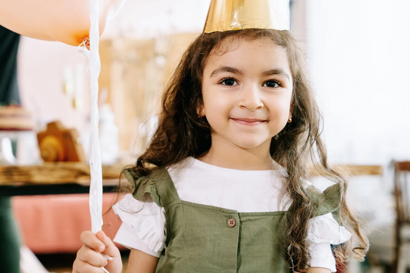 Adorable girl in a party hat holding a balloon at a festive celebration.